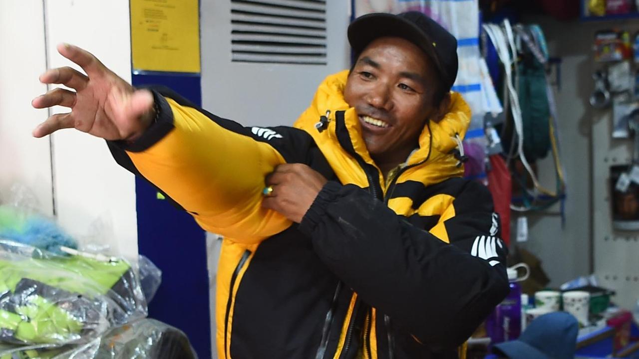 Der nepalesische Bergführer Kami Rita Sherpa trägt eine gelbe Jacke, lächelt freundlich und streckt seine Hand greifend nach links.