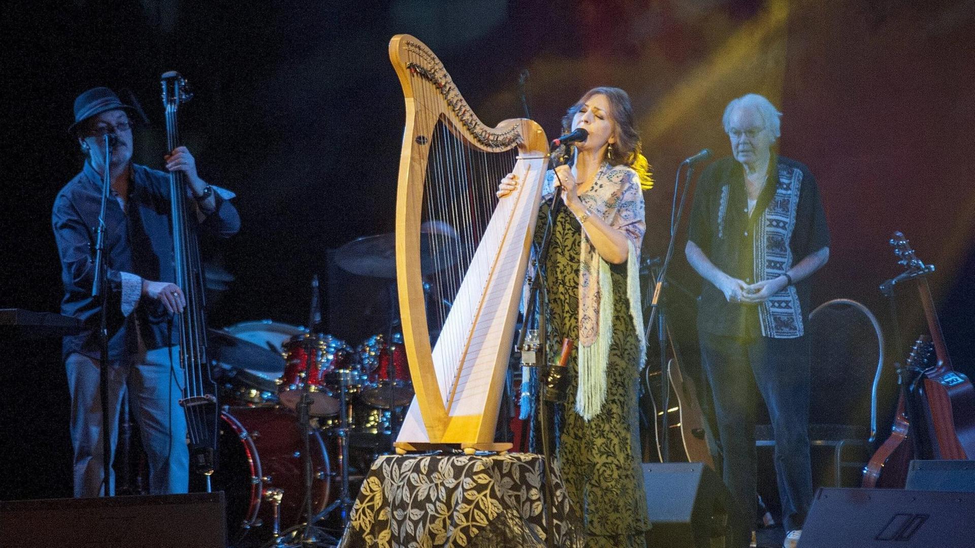 Eine Frau und zwei Männer stehen auf einer Bühne. Die Frau spielt eine Harfe.