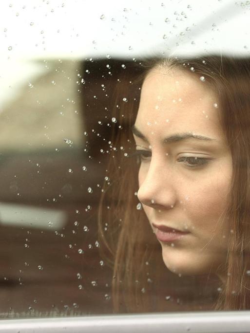 Eine junge Frau mit Kopfhörern blickt gedankenverloren aus einem Autofenster.