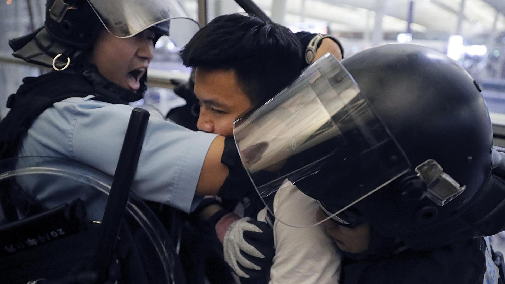 Polizisten in Schutzausrüstung nehmen einen Demonstranten im Hongkonger Flughafen fest.