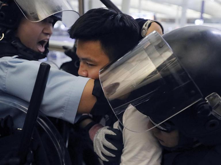 Polizisten in Schutzausrüstung nehmen einen Demonstranten im Hongkonger Flughafen fest.