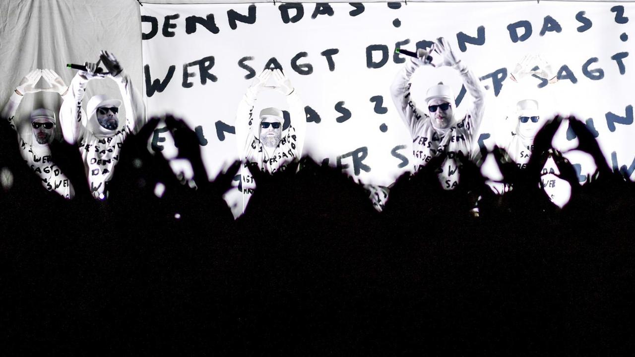Die Band "Deichkind" spielt am 20.09.2019 beim Reeperbahn-Festival auf einer Bühne vor dem Millerntorstadion in Hamburg. Die Musiker tragen alle weisse Kleidung und weiße Schminke. Schwarze Schrift "Wer sagt denn das?" steht hinter ihnen auf einem Banner. Die Menschenmenge vor ihnen streckt jubelnd die Arme in die Höhe.