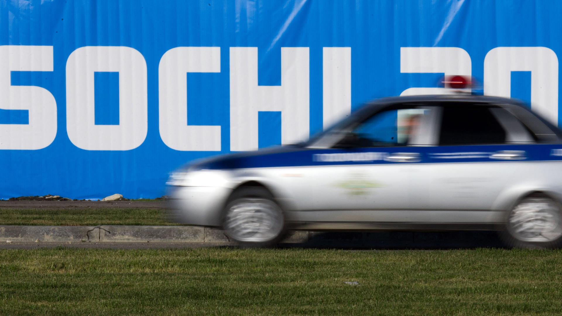 Ein Polizeiauto fährt in der Nähe des Olympischen Park im russischen Sotschi direkt am Schwarzen Meer an einem Werbebanner mit dem Schriftzug "Sochi 2014" vorbei.