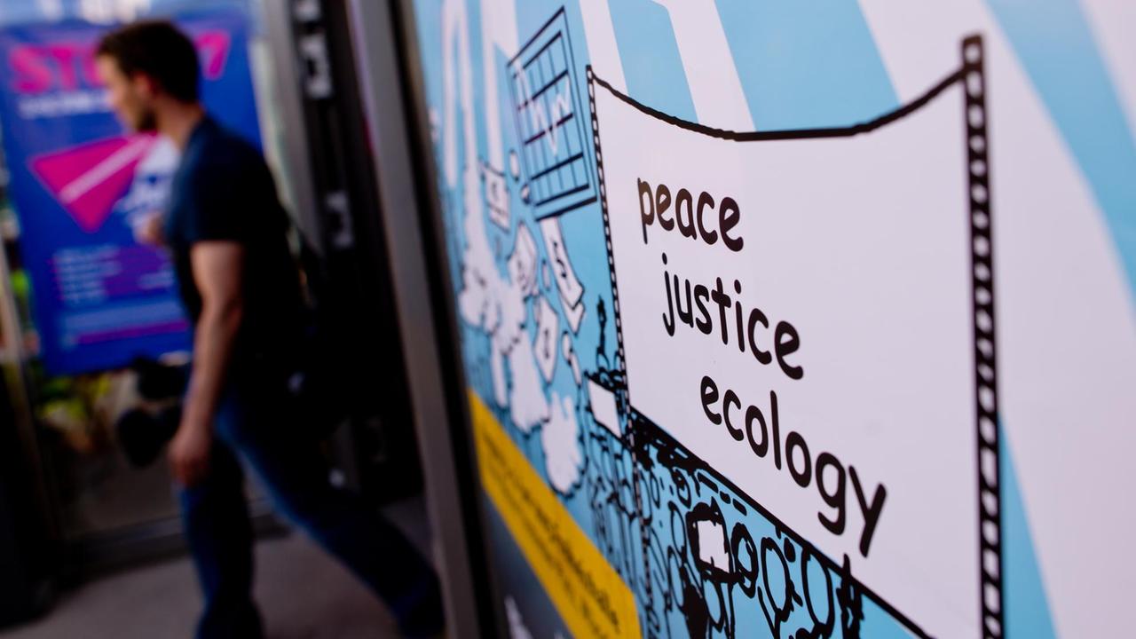 Ein Plakat mit der Aufschrift "peace, justice, ecology" ist am 03.06.2015 in München (Bayern) beim internationalen "Gipfel der Alternativen" zu sehen. Die Teilnehmer des Alternativgipfels werfen den großen Wirtschaftsnationen des G7-Gipfels eine Mitverantwortung an den globalen Krisen und dem sozialen und ökologischen Ungleichgewicht auf der Welt vor
