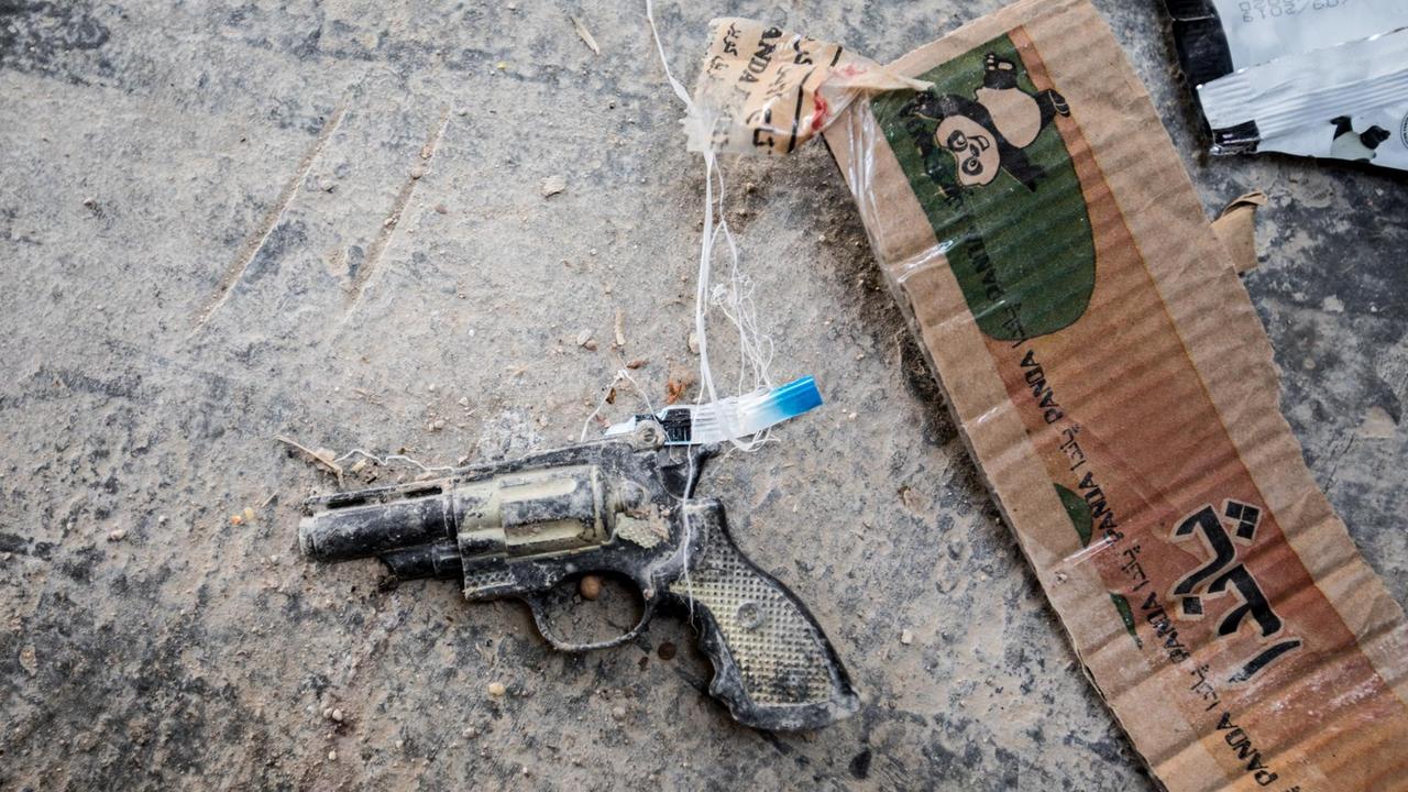 Auf dem Boden im al-Hawl Camp liegt eine vergessenen Kinderspielzeugpistole, daneben ein Stück Pappe, aus das arabische Schriftzeichen aufgedruckt sind.