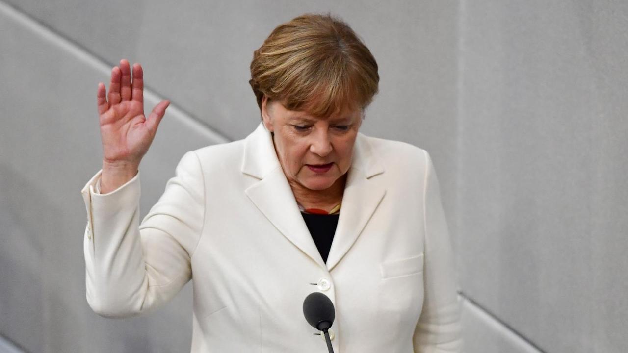 Merkel steht mit erhobener Hand im Bundestag.