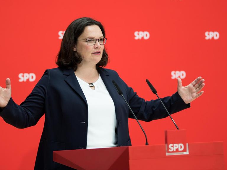Andrea Nahles, Vorsitzende der Sozialdemokratischen Partei Deutschlands, SPD, steht mit offenen Armen an einem Rednerpult vor einem roten Hintergrund mit SPD-Logo.