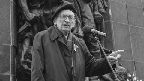Wladyslaw Bartoszwski spricht in ein Mikrofon vor dem Mahnmal des Warschauer Ghettos.