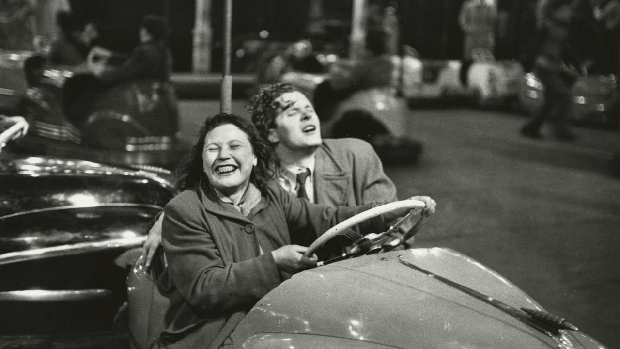 Eine Frau und ein Mann fahren freudestrahlend mit geschlossenen Augen Autoscooter. Die Fotografie ist schwarz-weiß.