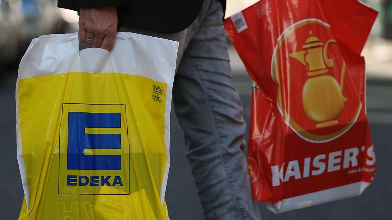Ein Mann geht mit jeweils einer Tüte von Edeka und Kaiser's über die Straße.