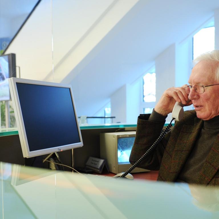 Ein Senior sitzt im Büro an einem Empfang und telefoniert.