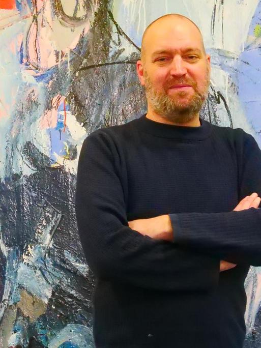 Felix Scharlau - Autor des Romans "Du bist es vielleicht" - vor einem bunten Gemälde im DLF-Funkhaus