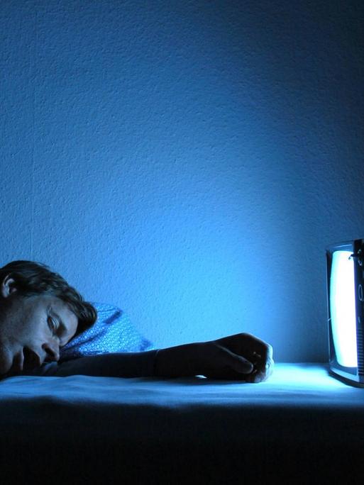 Man liegt mit geschlossenen Augen vor einem eingeschalteten Fernseher