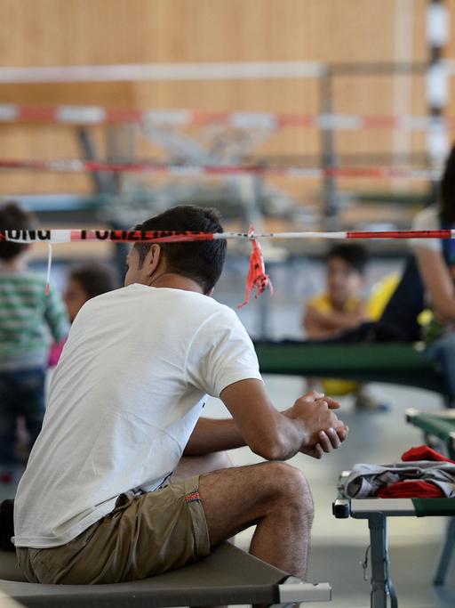 Flüchtlinge sitzen am 04.08.2015 auf Feldbetten in einer Turnhalle auf dem Gelände der Bundespolizei in Rosenheim.