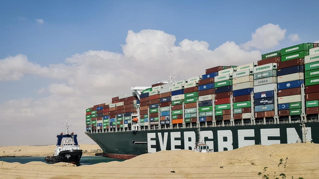 Blick vom Ufer auf das mit hunderten Containern beladene Schiff; daneben der Schlepper. Auf dem Schiff steht in großen weißen Buchstaben "Evergreen"