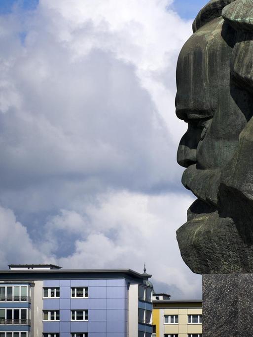 Karl-Marx-Denkmal in Chemnitz, dahinter ein Hausdächer und ein bewölkter Himmel.