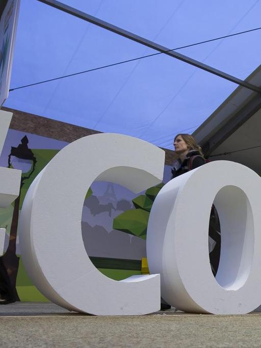 Ein Mann läuft an den etwa einen Meter hohen Zeichen "#COP21" vorbei, die als Installation im Raum stehen.