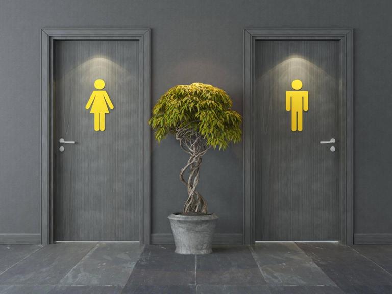 Zwei Türen mit jeweils einem gelben Zeichen, welches für Männer oder Frauen stehen soll. Dazwischen steht eine Pflanze.