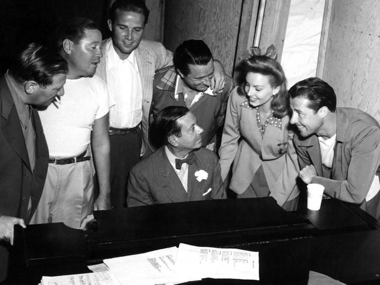 Cole Porter sitzt am Piano, um ihn herum stehen von links nach rechts Gregory Ratoff, Jack Oakie, Jaye Martin, William Gaxton, Janet Blair und Don Ameche