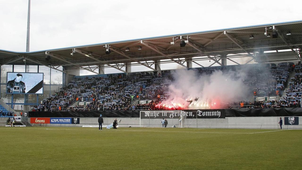 Eine Tribüne im Chemnitzer Fußballstadion. Zu sehen ist ein Banner mit der Aufschrift "Ruhe in Frieden, Tommy". Auf der Videoleinwand: das Gesicht von Thomas Haller