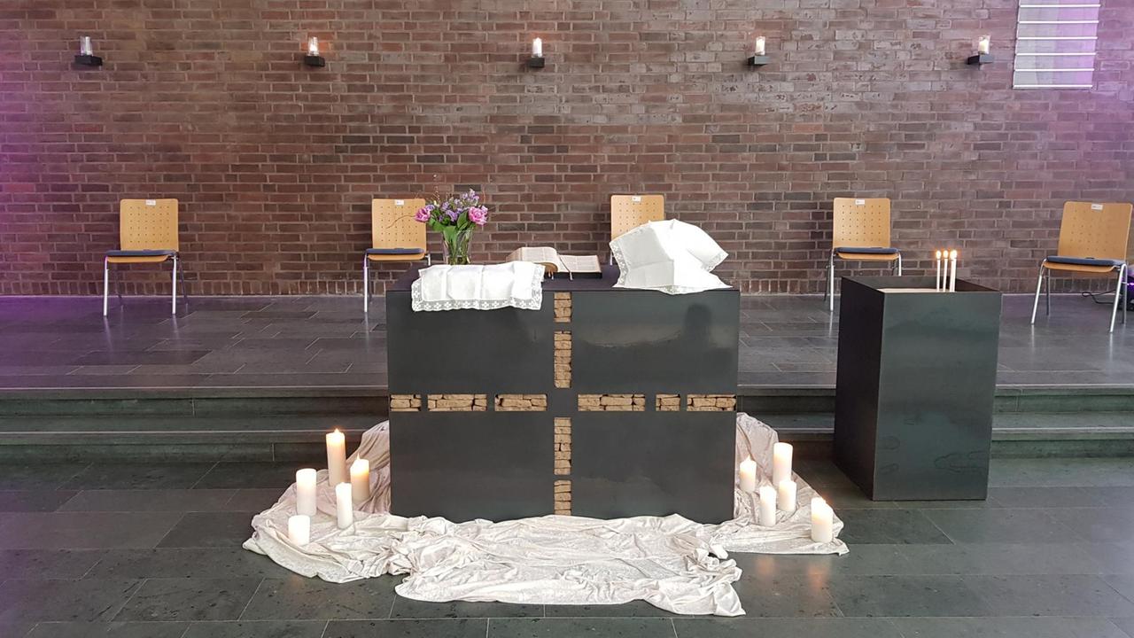 Bild eines schlichten Altars in magentafarbenes Licht getaucht. Mehrere Kerzen sind aufgestellt.