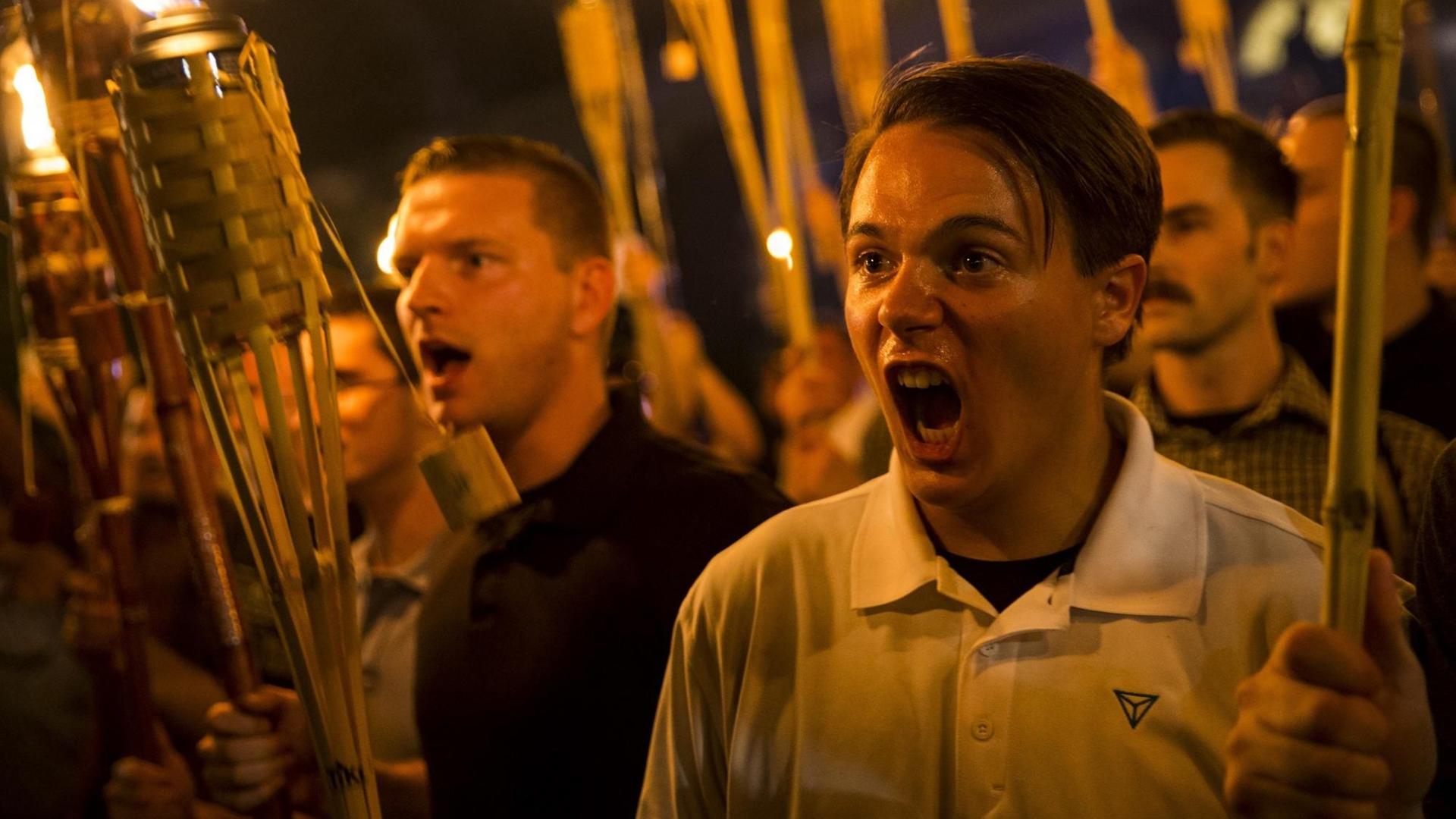 Ein Mann schreit in einer Gruppe von Demonstranten bei einem Fackelmarsch.
