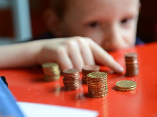 Ein fünfjähriger Junge sitzt an einem roten Tisch und zählt sein gespartes Taschengeld