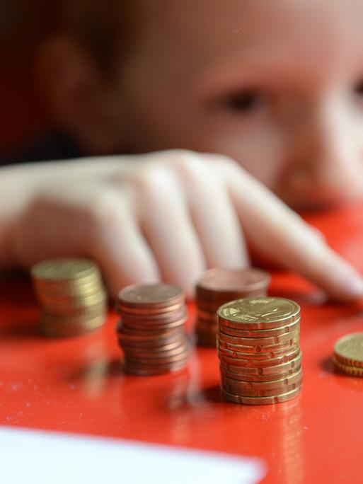 Ein fünfjähriger Junge sitzt an einem roten Tisch und zählt sein gespartes Taschengeld