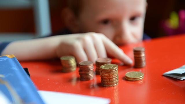 Ein fünfjähriger Junge sitzt an einem roten Tisch und zählt sein gespartes Taschengeld