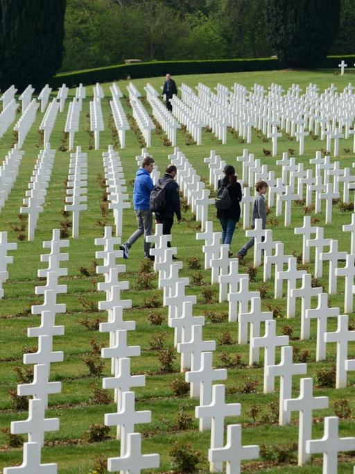 Besucher gehen zwischen den Grabkreuzen auf dem französischen Soldatenfriedhof am Beinhaus von Douaumont (Hintergrund) aus dem Ersten Weltkrieg nahe Verdun/Frankreich (Region Lorraine), aufgenommen am 25.04.2014.
