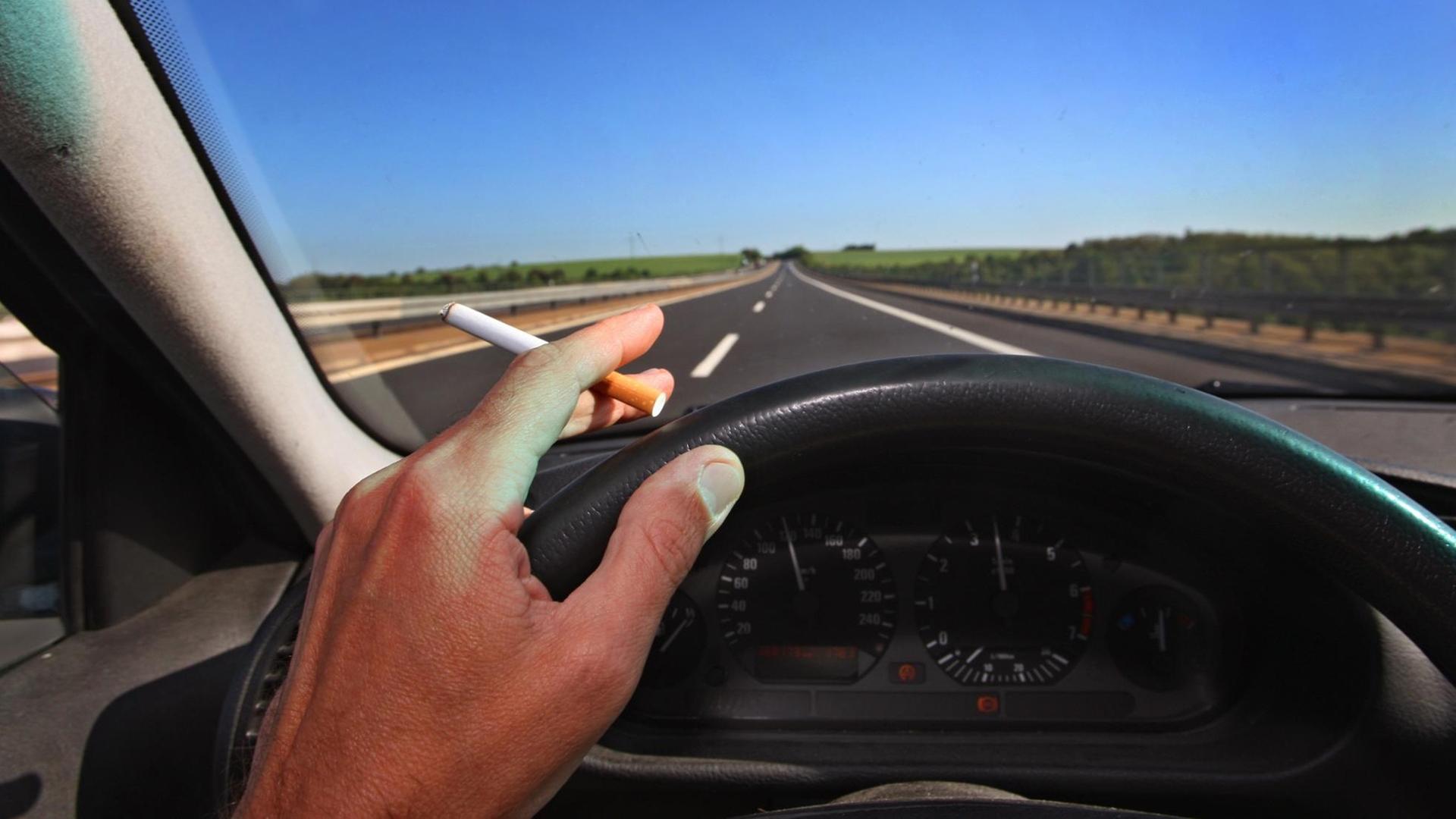 Ein Mann raucht während des Autofahrens eine Zigarette. Man sieht das Lenkrad und seine Hand mit Zigarette. Ein Mann raucht während des Autofahrens eine Zigarette. Man sieht das Lenkrad und seine Hand mit Zigarette.