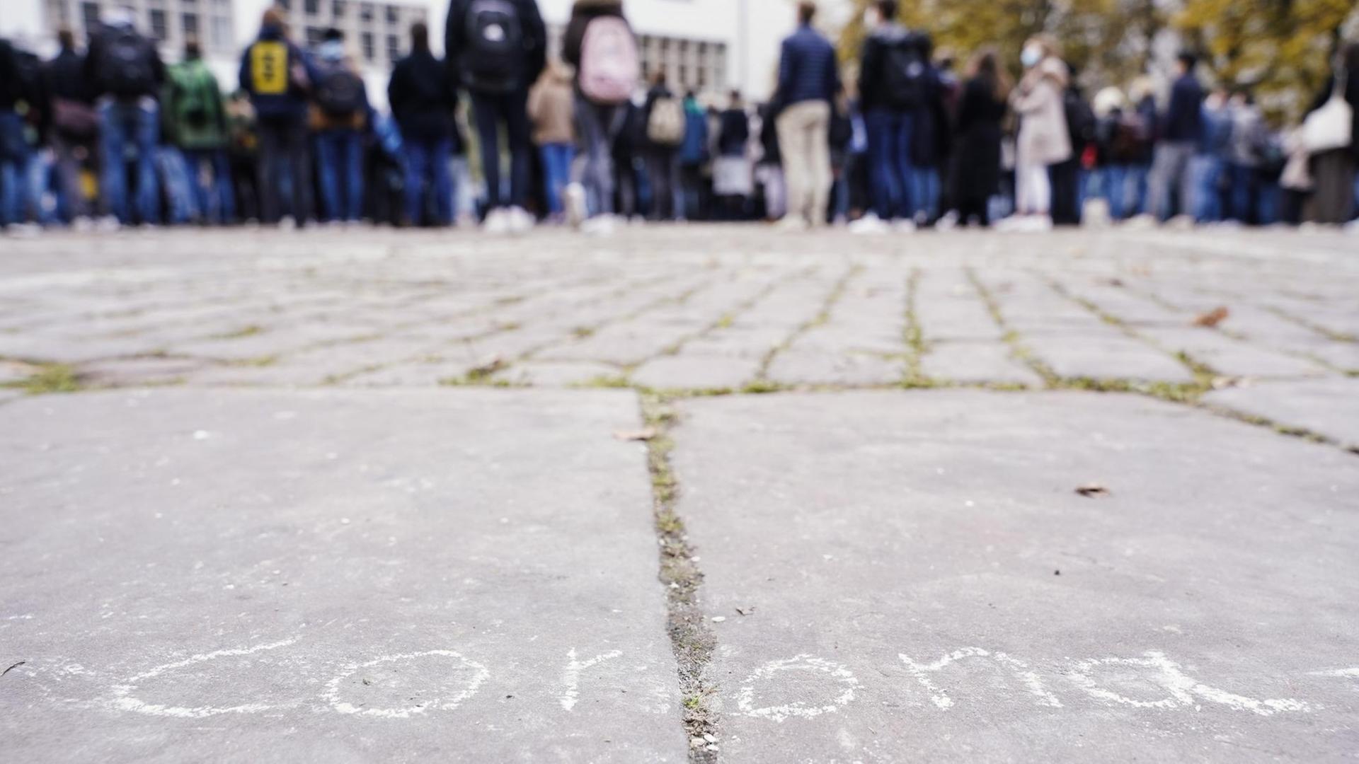 Erstsemester-Studenten stehen bei einer Willkommensveranstaltung auf dem Universitätsplatz vor dem Gebäude der Neuen Universität hinter dem mit Kreide auf dem Boden aufgemalten Schriftzug "corona"