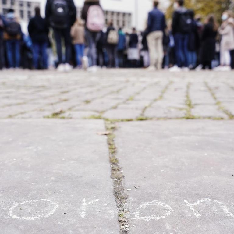 Erstsemester-Studenten stehen bei einer Willkommensveranstaltung auf dem Universitätsplatz vor dem Gebäude der Neuen Universität hinter dem mit Kreide auf dem Boden aufgemalten Schriftzug "corona"