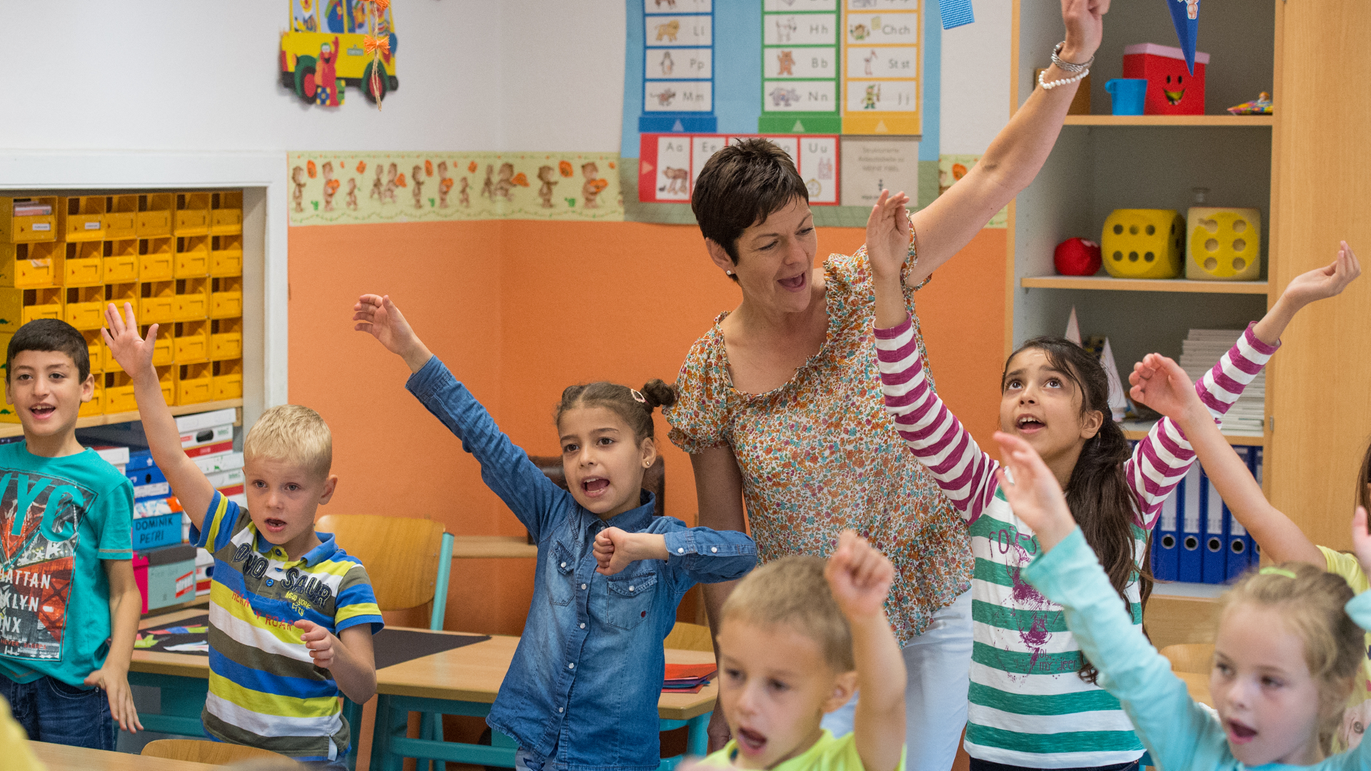 Grundschulkinder und die Schulleiterin singen und bewegen ihre Arme.