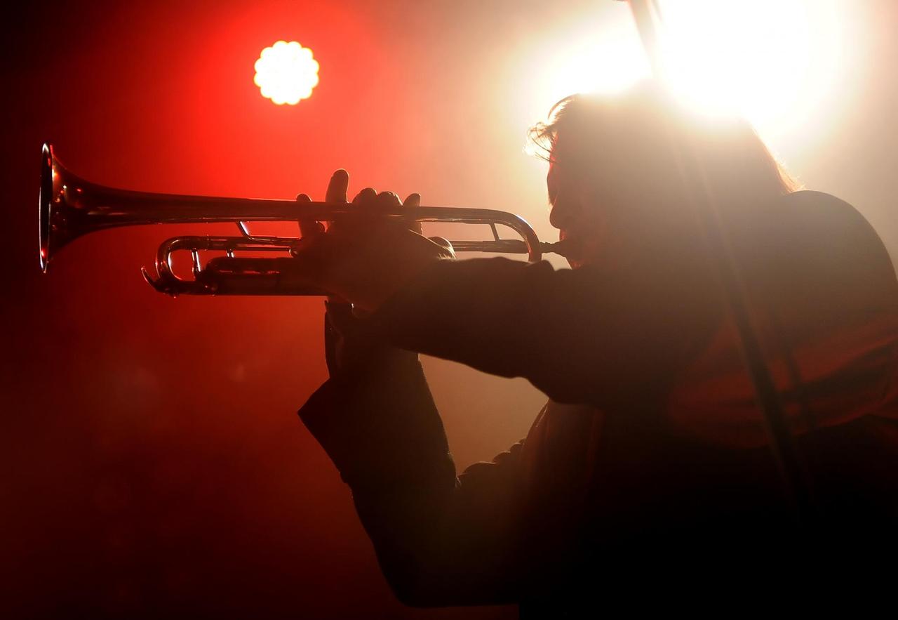 Ein Mann spielt Trompete auf einem Konzert. Er ist dunkel, weil das rote Licht hinter ihm hell scheint.