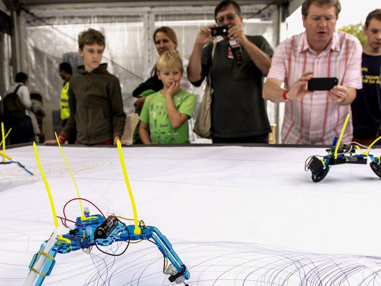 SYMBOLBILD - Besucher der "Word Maker Fair", einer zweitätigen Messe für Do-it-yourself-Innovationen, stehen im Jahr 2013 in New York an einem Tisch, auf dem Roboter zeichnen.