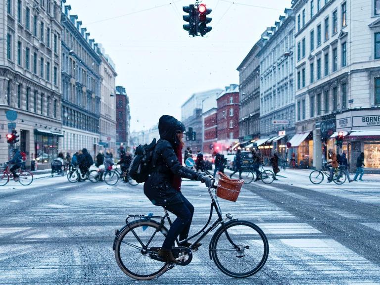 Eine Frau fährt mit dem Rad über eine verschneite Kreuzung.