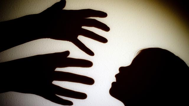 Der Schatten von einer Hand von einer erwachsenen Person und der Kopf von einem Kind an einer Wand von einem Zimmer.