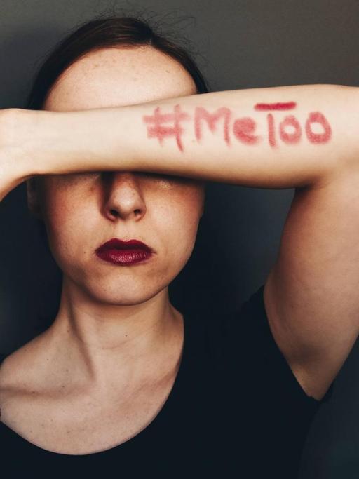 Eine Frau hält sich einen Arm vor das Gesicht, auf dem mit roter Farbe geschrieben steht: MeToo