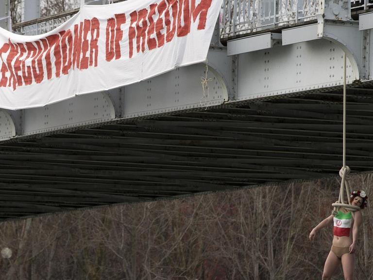 Proteste in Paris: Eine Femen-Aktivisten ließ sich in Anspielung auf die Hinrichtungen im Iran von einer Brücke über der Seine hängen. Auf einem Transparente daneben steht: "Willkommen Rohani, Henker der Freiheit."