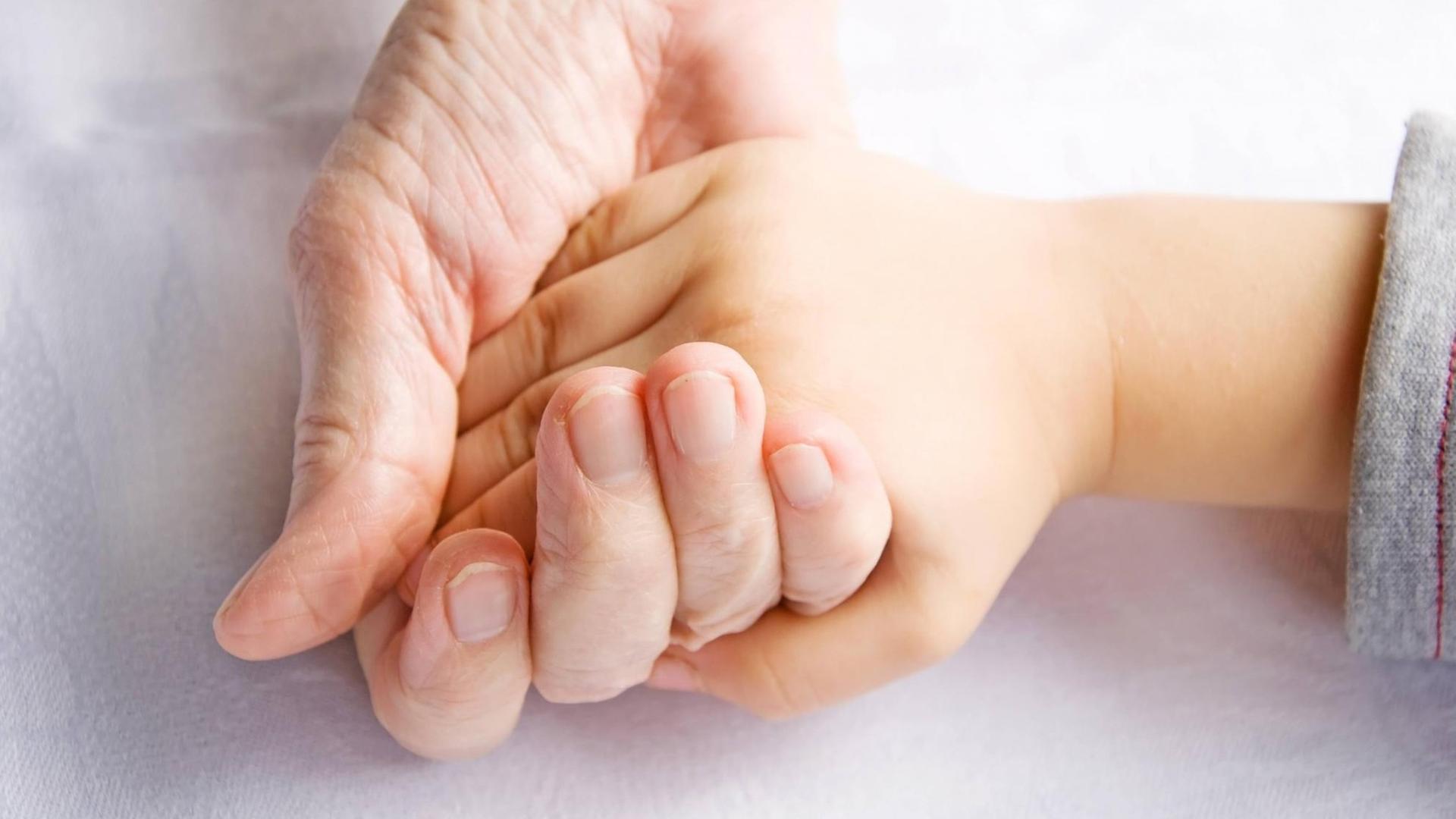 Hand einer älteren Person hält eine Kinderhand.