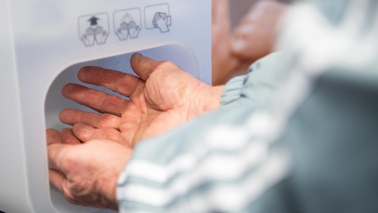 Ein Mann desinfiziert im Eingangsbereich einer Klinik seine Hände. 