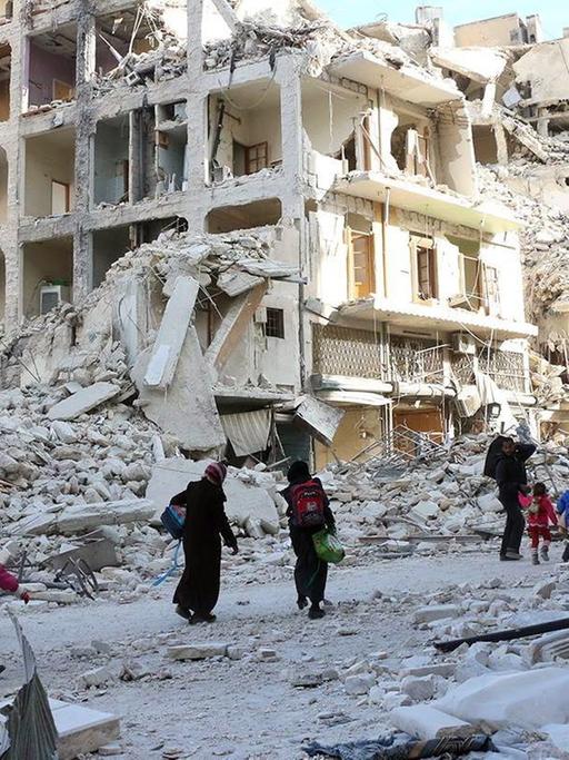 Syrische Familien auf der Flucht aus Ost-Aleppo - im Hintergrund sind zerstörte Gebäude zu sehen.