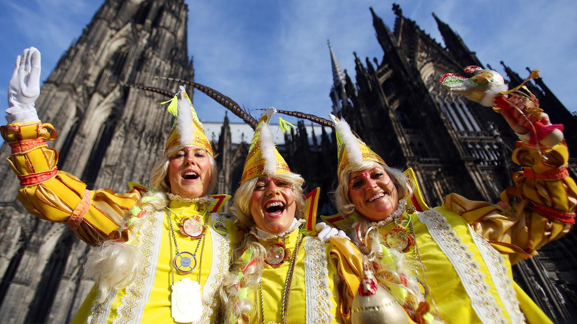 Drei Karnevalistinnen stehen vor dem Kölner Dom.