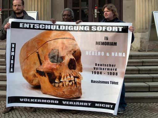 Demonstranten mit einem Transparent "Entschuldigung sofort - Völkermord verjährt nicht" vor einem Gebäude der Charite in Berlin