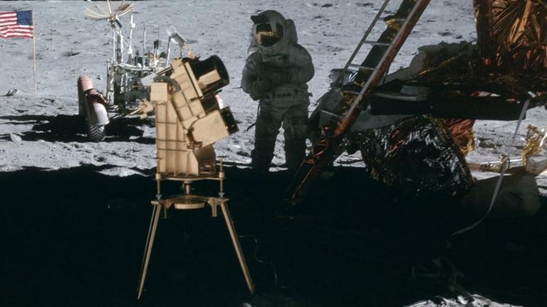 Astronauten neben Landestelle von Apollo 16 auf dem Mond, daneben die UV-Kamera