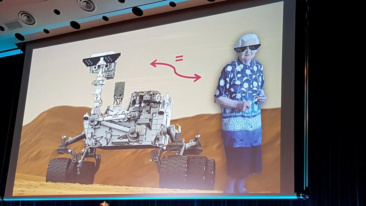 Eine Folie aus dem Vortrag von Felix Büsching zeigt dem Mars-Rover und eine alte Frau, beide mit Sonnenbrille.