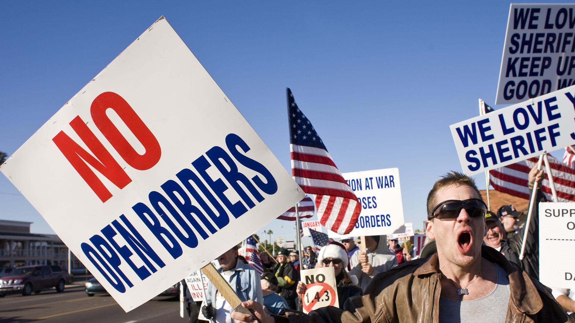 Demonstration in Phoenix gegen Immigration in die USA. "No open borders" steht auf einem Protestplakat, amerikanische Flaggen werden geschwungen.