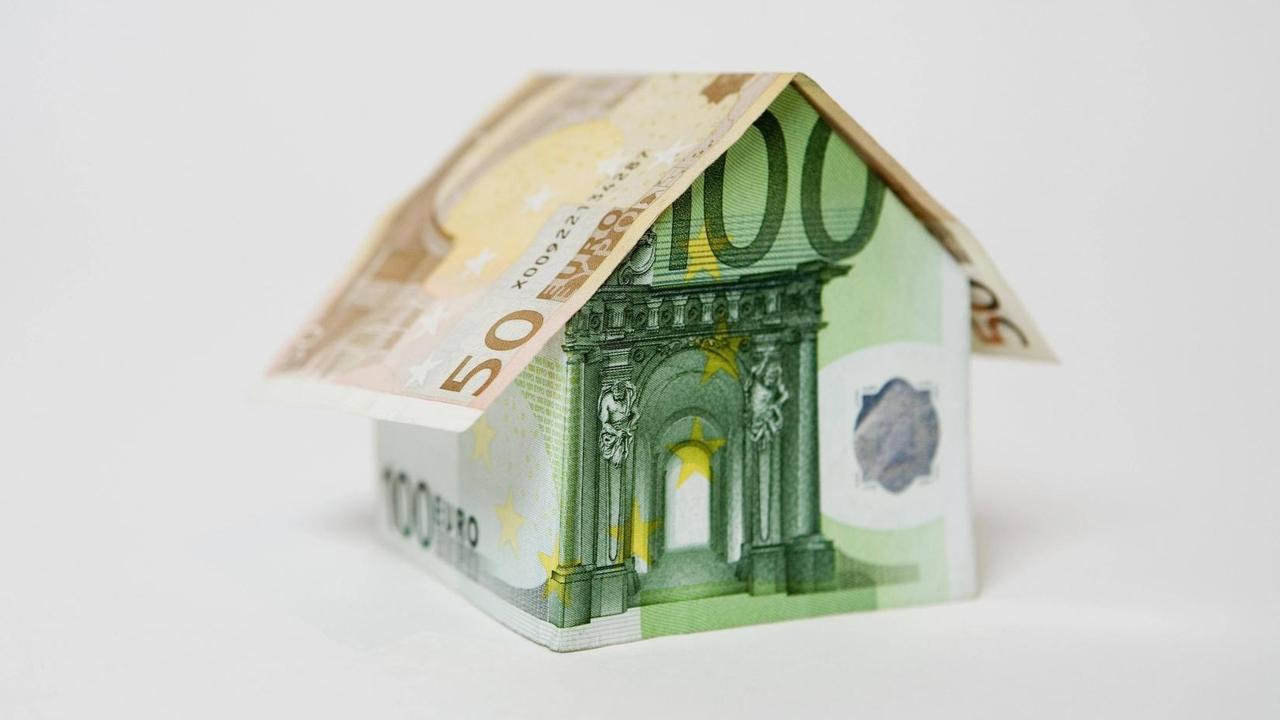 Das Symbolbild zeigt mehrere Euro Banknoten, die zu einem Haus gefaltet sind.