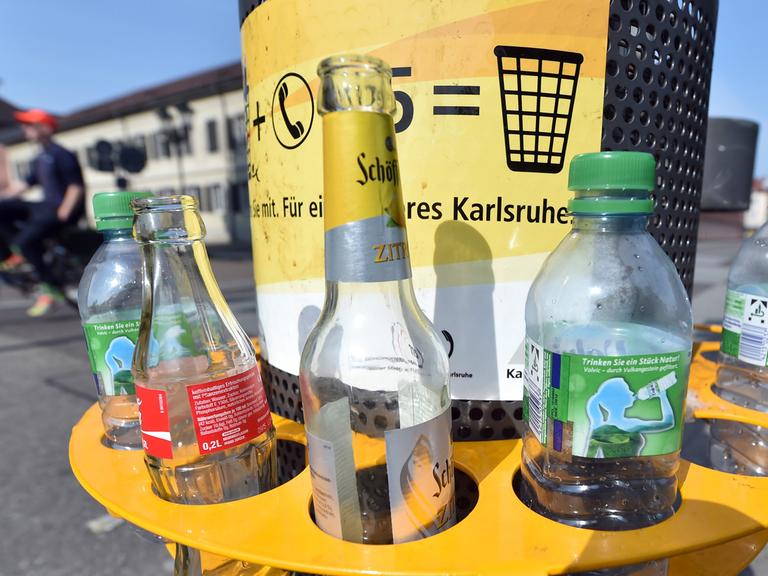An einem Mülleimer in der Innenstadt von Karlsruhe (Baden-Württemberg) ist am 06.08.2014 ein Pfandring angebracht in dem leere Flaschen stehen. Wer seine Pfandflaschen oder -dosen nicht ins Geschäft zurückbringen möchte, kann sie in die Ringe stecken. So ist es Pfandsammlern einfacher möglich, die Flaschen und Dosen mitzunehmen.